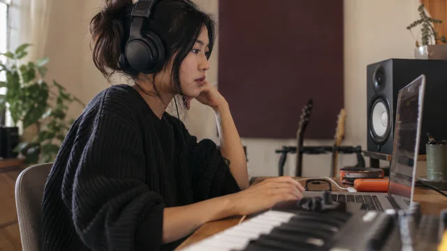 A musician listening carefully to a track on headphones at a home studio